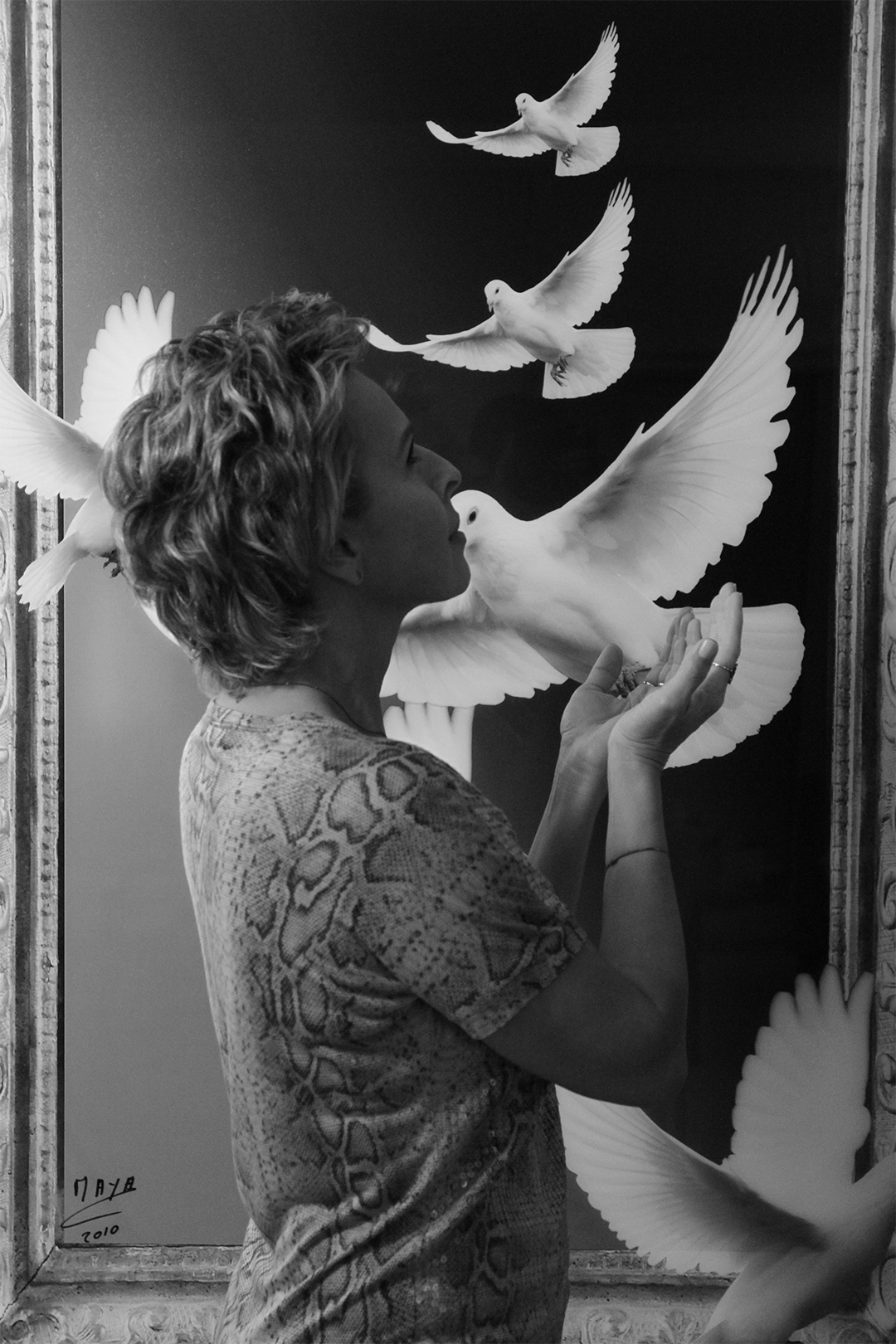 Photographie en noir et blanc de la créatrice Maria Dowlatshahi devant un tableau représentant des colombes.