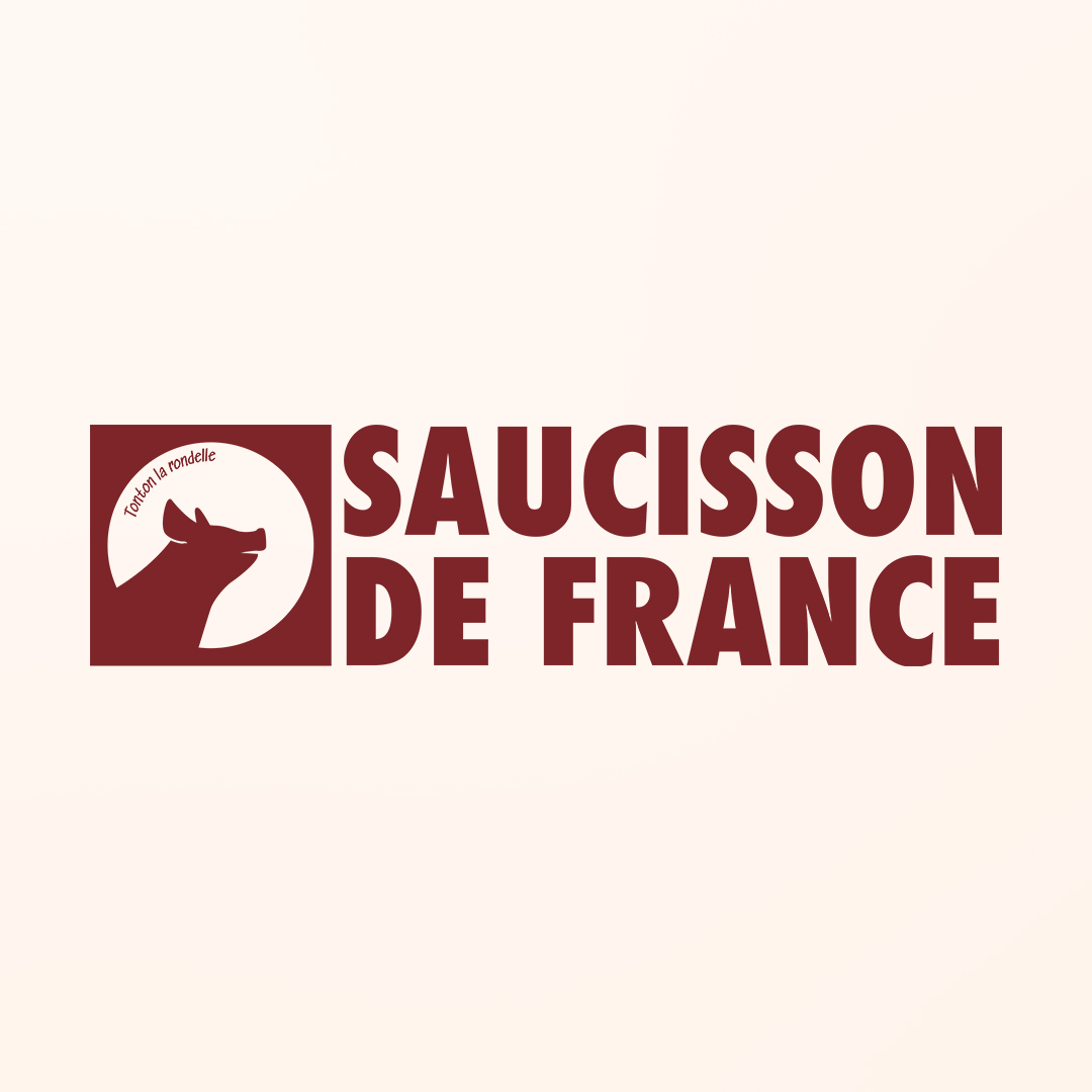 Logo de Saucisson de France, intégré sur une enseigne carrée fixée sur une façade. Le logo est en blanc, gravé sur fond bordeaux ;  la mention "Saucisson de France" est inscrite en lettres capitales, sur deux lignes en dessous du carré représentant le cochon.