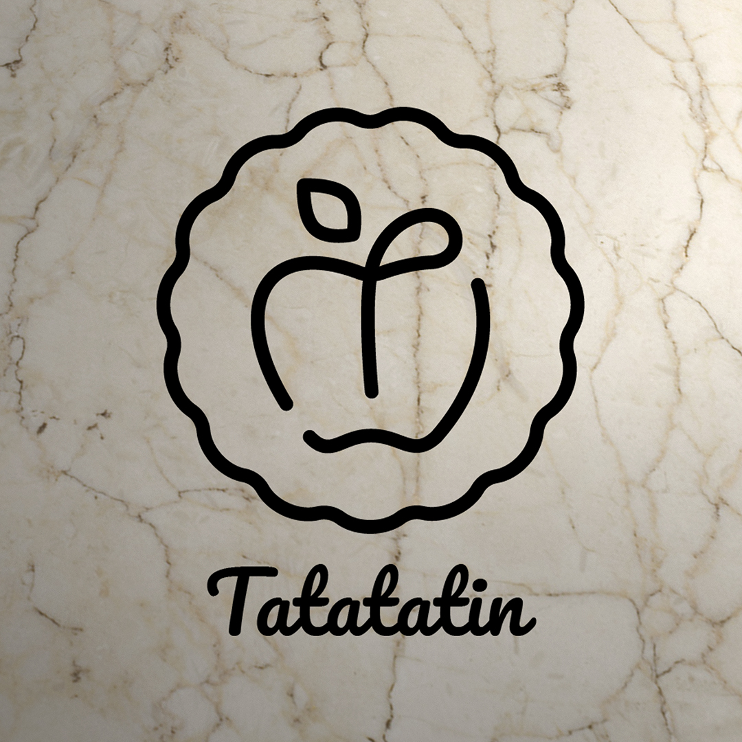 Logo du restaurant Tatatatin : il s'agit d'un logo circulaire en forme de plat à tarte en ligne noire sur fond de marbre blanc. À l'intérieur du cercle une pomme dont le dessus se transforme en T pour former l'initiale de Tatatatin. En dessous du cercle le mot Tatatatin écrit en typographie manuscrite.