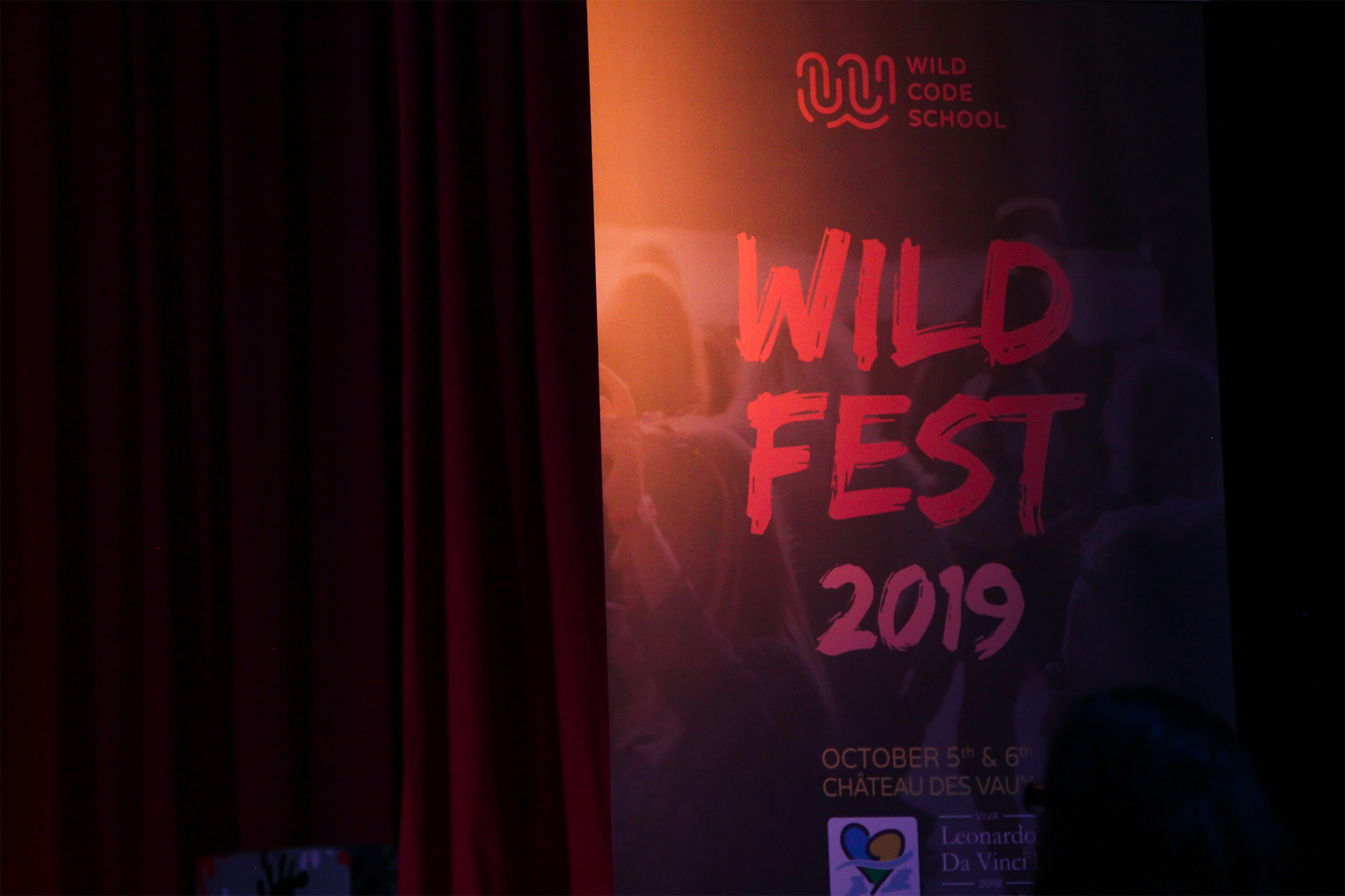 Photographie du kakemono de l’événement Wild fest devant un rideau rouge.