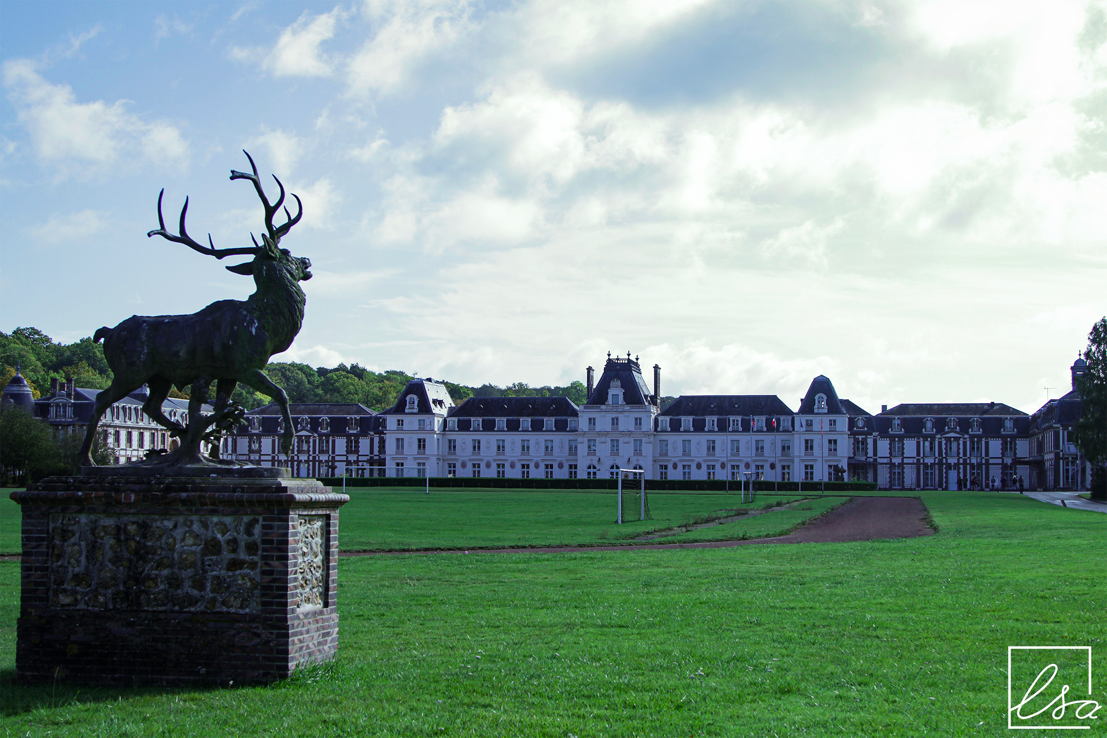 Photographie d'une statue de cerf située dans les jardins du Château des Vaux, avec le bâtiment en arrière plan.